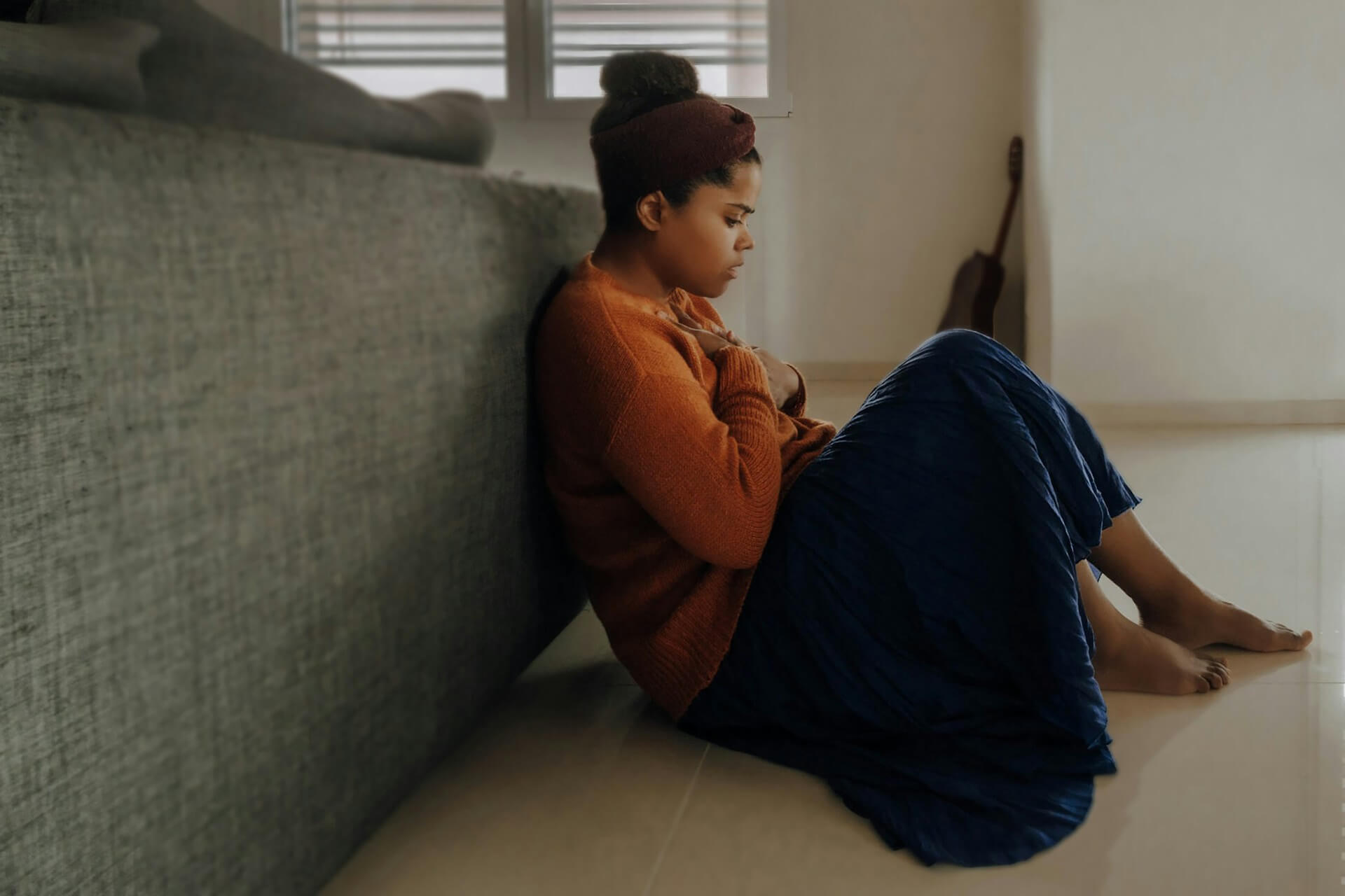 woman sat on the floor holding her chest looking sad