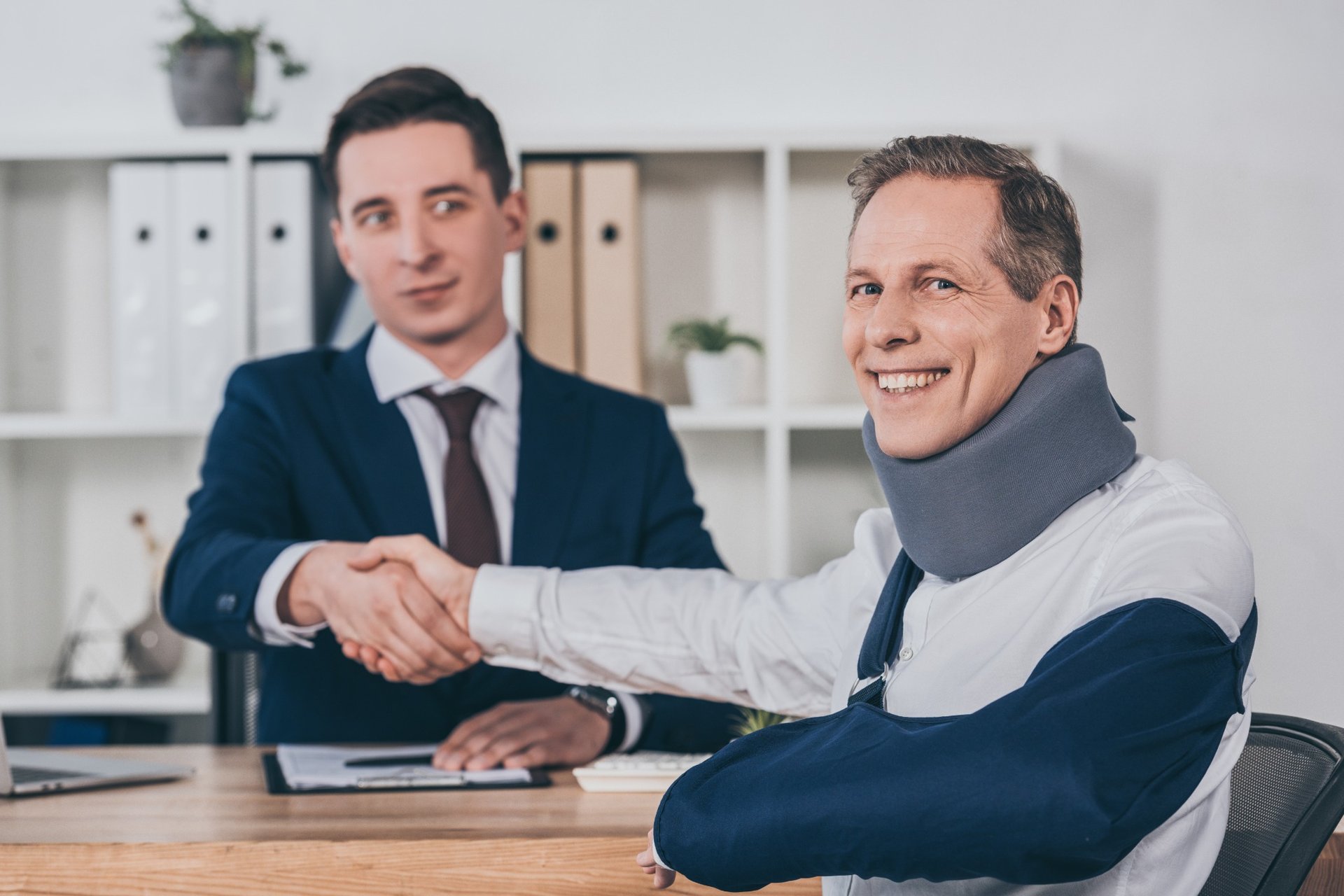 Injured man in neck brace shaking hands with lawyer