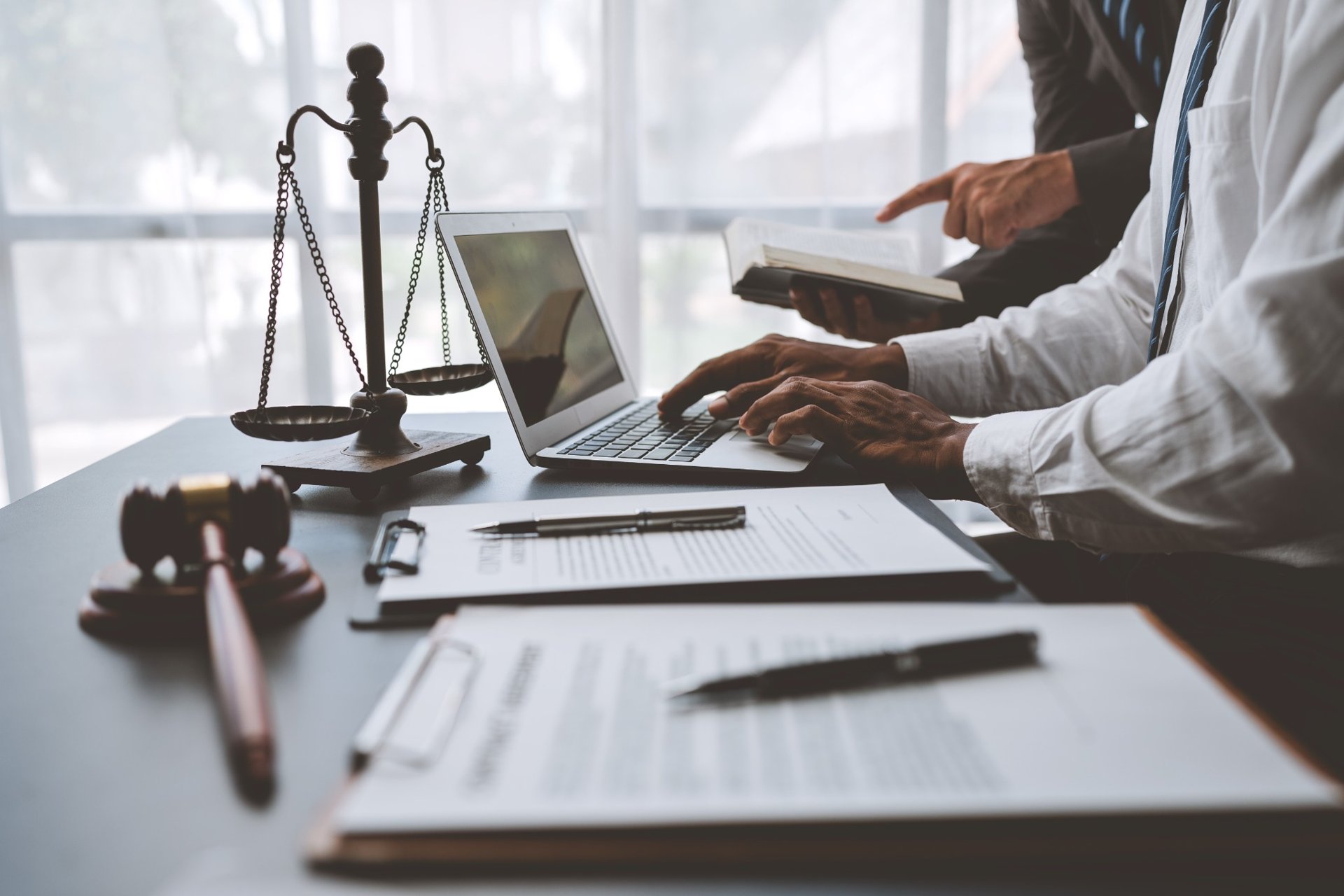 Lawyer typing on laptop next to justice scale and legal documents