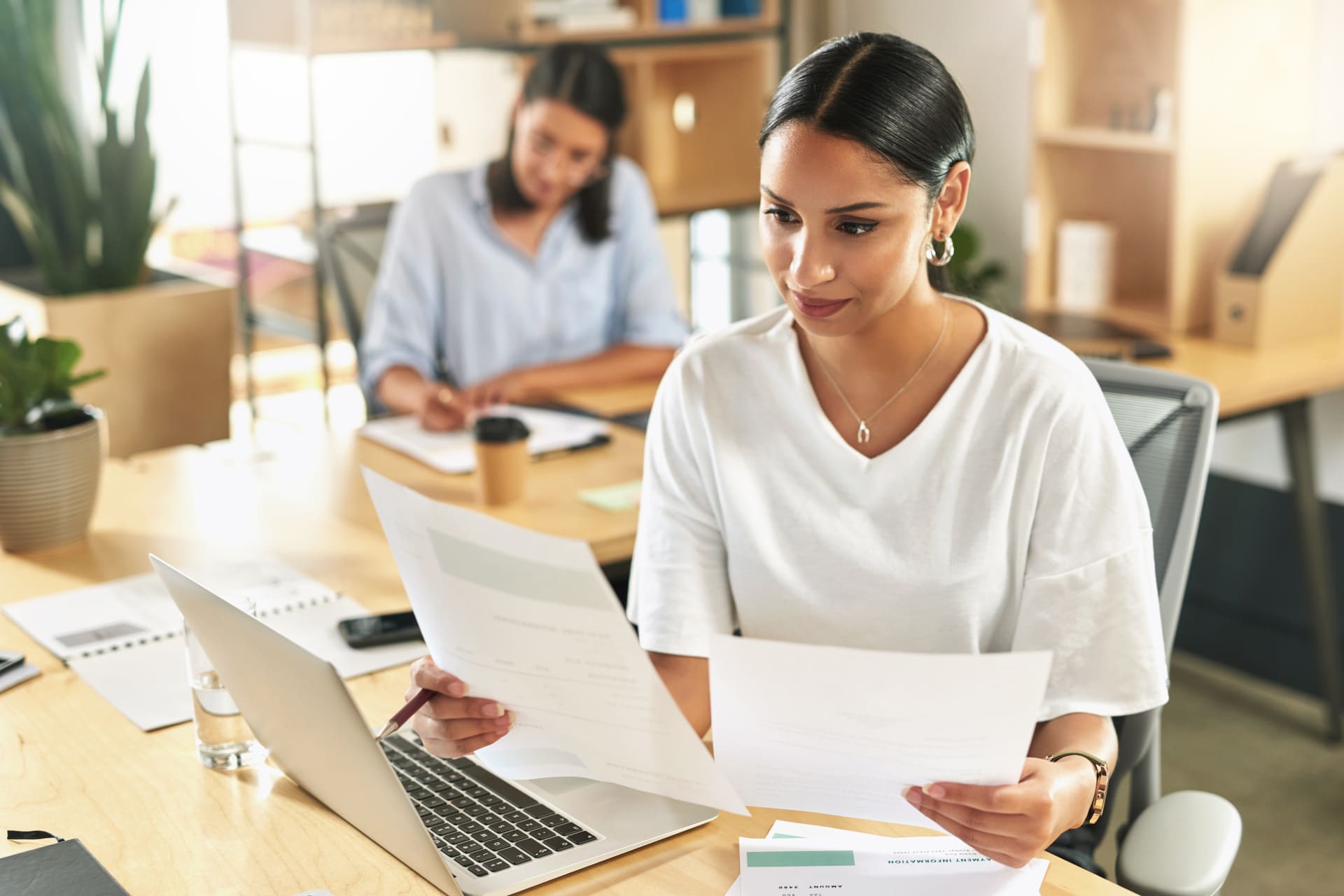 Woman analyzing paperwork and reports while working on a laptop at the office