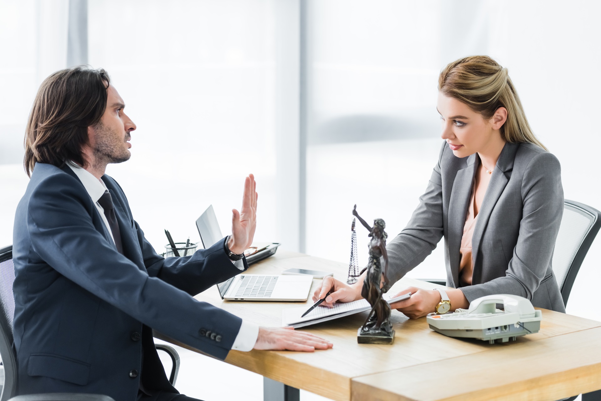 Male client in a suit raising his hand to decline while consulting with a female lawyer at her office desk
