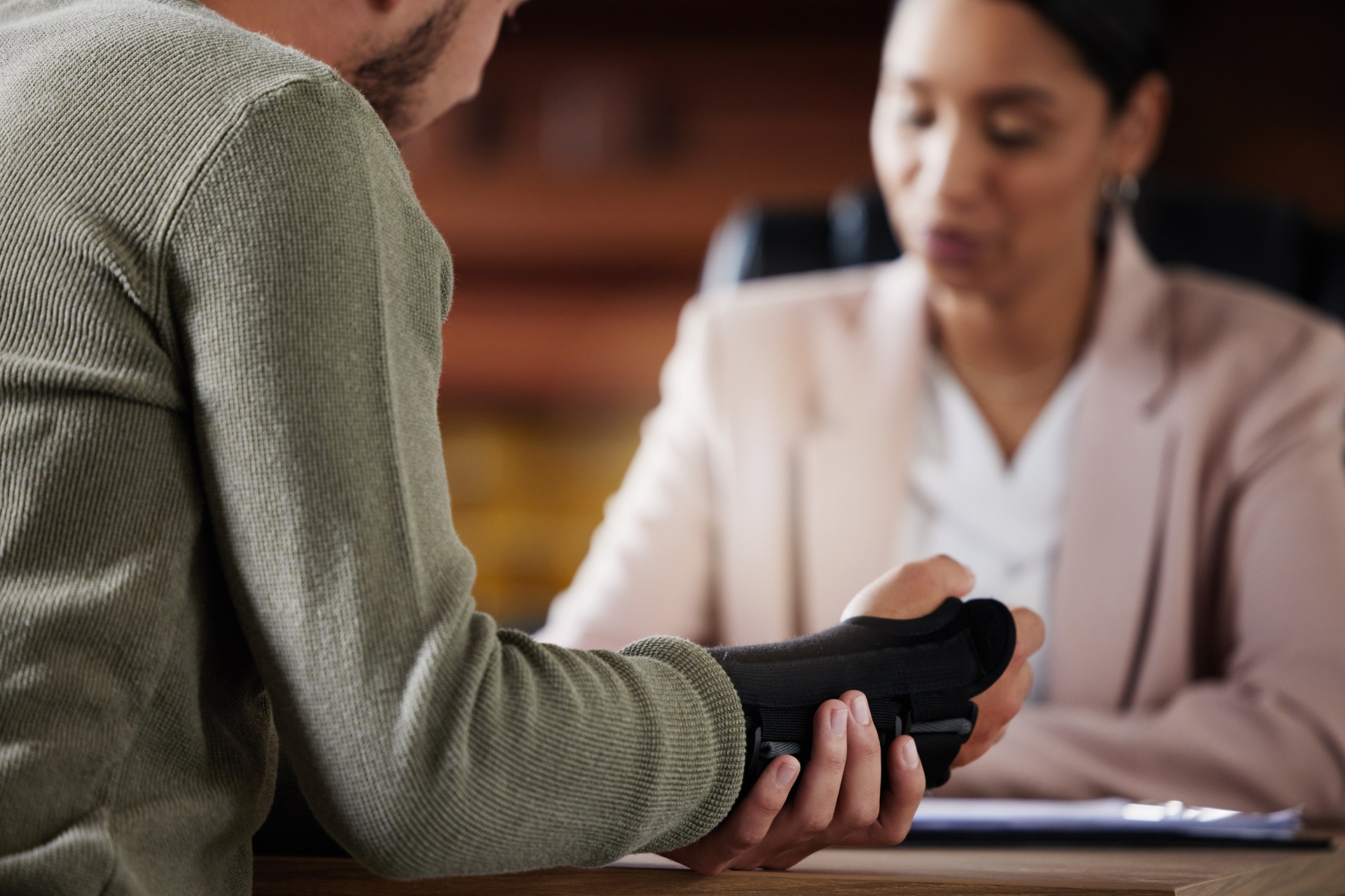 Close-up of an injured man showing his hand in a black wrist brace while speaking with a lawyer in an office