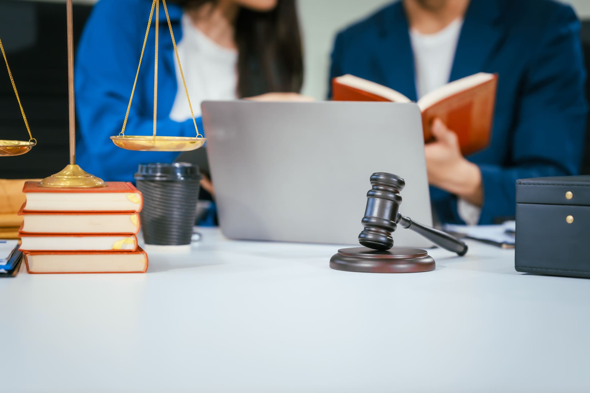 Two lawyers, a man and a woman, working together at a desk with law books, a gavel, a laptop, and a coffee cup